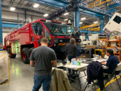 A group of people surrounding an Oshkosh striker vehicle in a warehouse