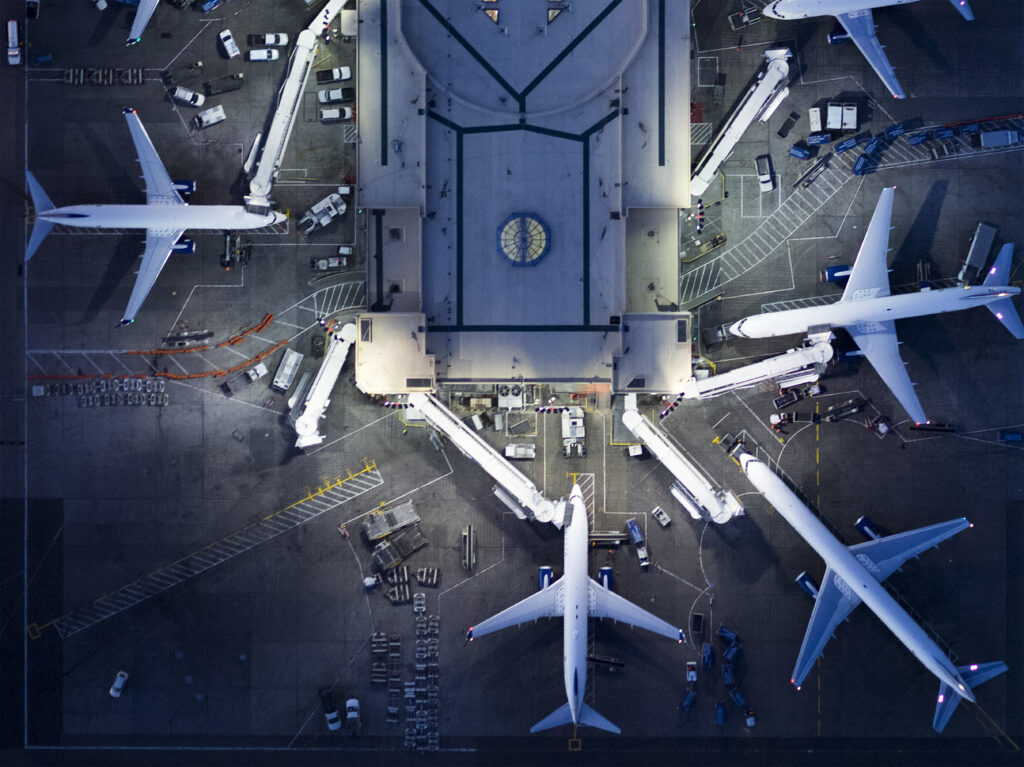 An aerial view of 5 airplanes parked around an airport terminal