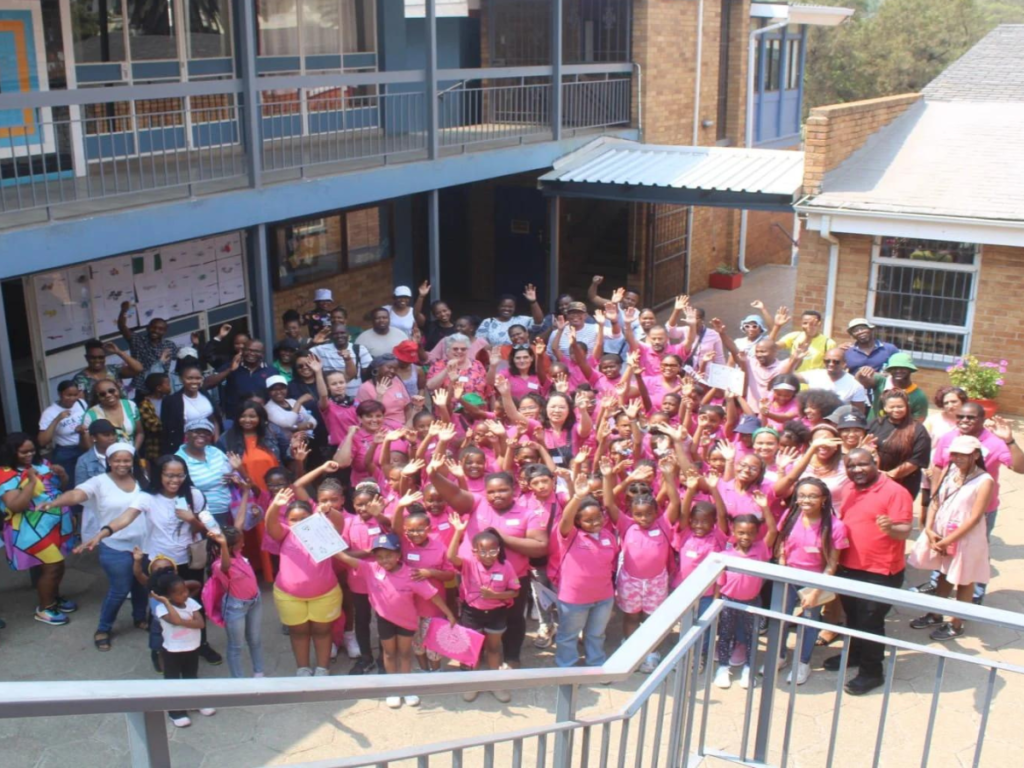 A group of women in pink shirts wave at the camera