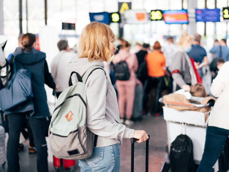 Stock image of a woman wearing a backpack, waiting in line at airport check-in