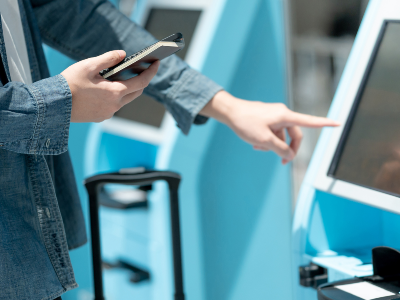 Stock image of a passenger holding their passport in one hand and using a touch screen security check point with the other hand