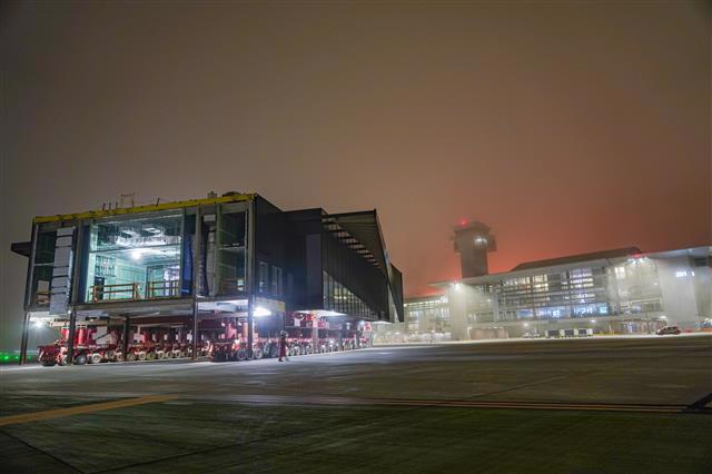 A segment of the Midfield Satellite Concourse South makes its way to the final project site for assembly and continued construction activities