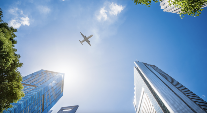 View from the ground of a plane flying over skyscrapers, blue sky