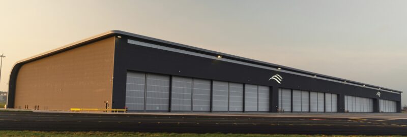 An aircraft hanger at an airport, brown walls and grey sliding hangar doors along the front