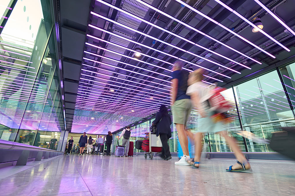 Passengers at London Heathrow Airport in part of terminal with coloured ceiling lights