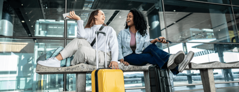 Two women smiling whilst sitting down with baggage
