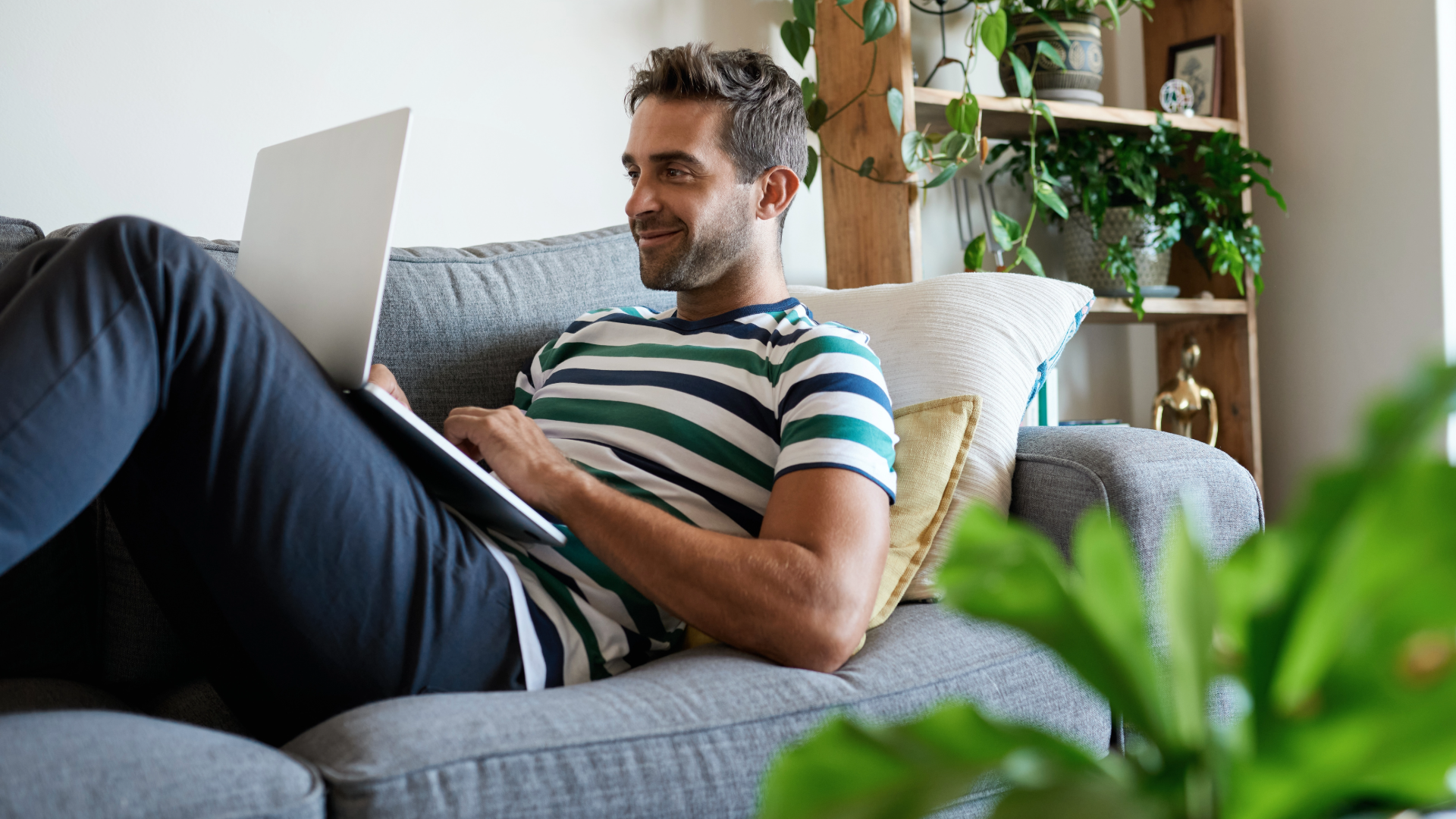 A man laying on a sofa on a laptop