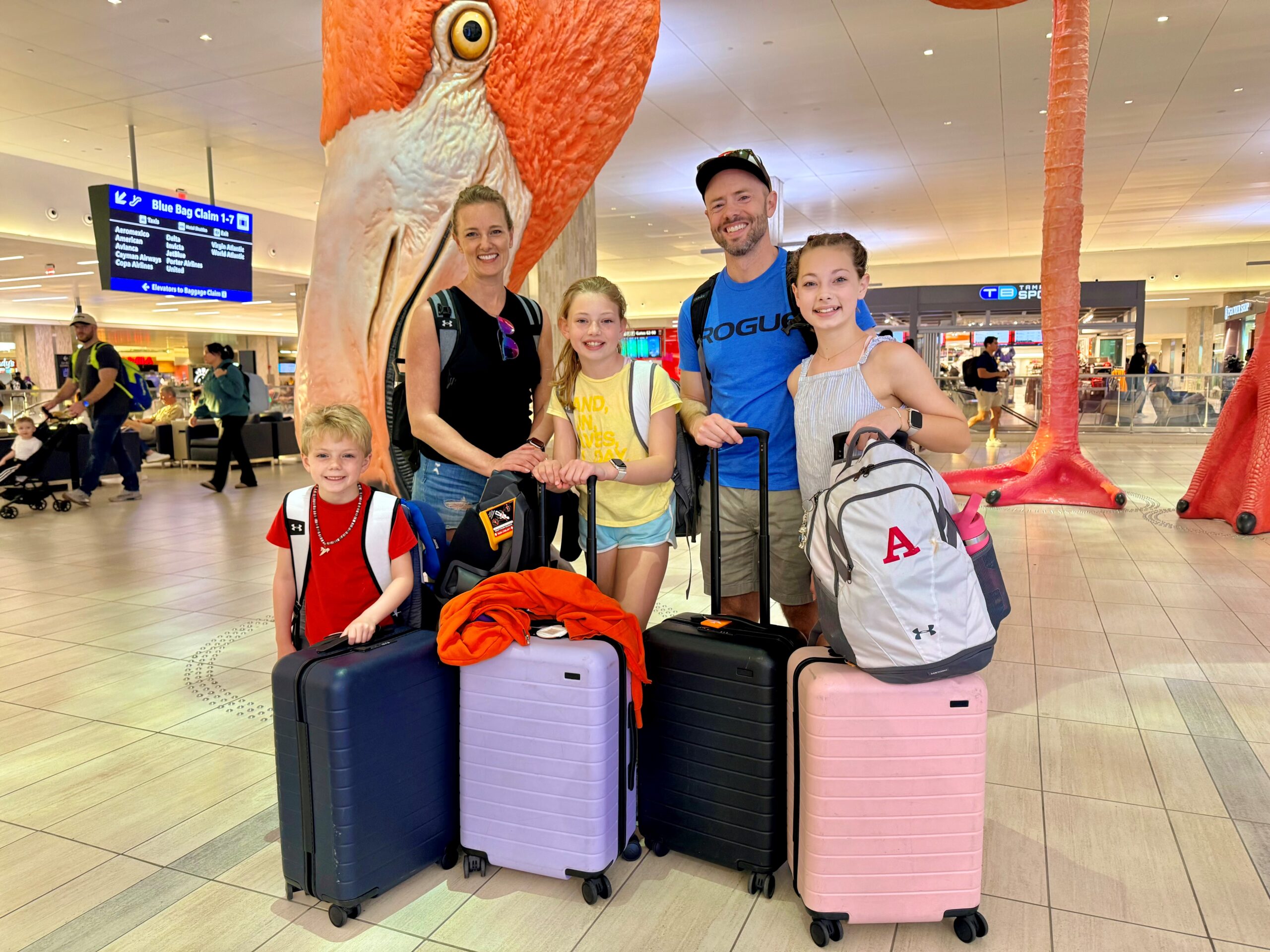 A family at an airport with luggage, also a big flamingo