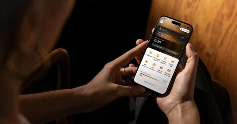 Someone holding a smartphone displaying a loyalty app screen, showing a membership card with a points balance and a grid of reward and service icons, with a warm wooden interior in the background.